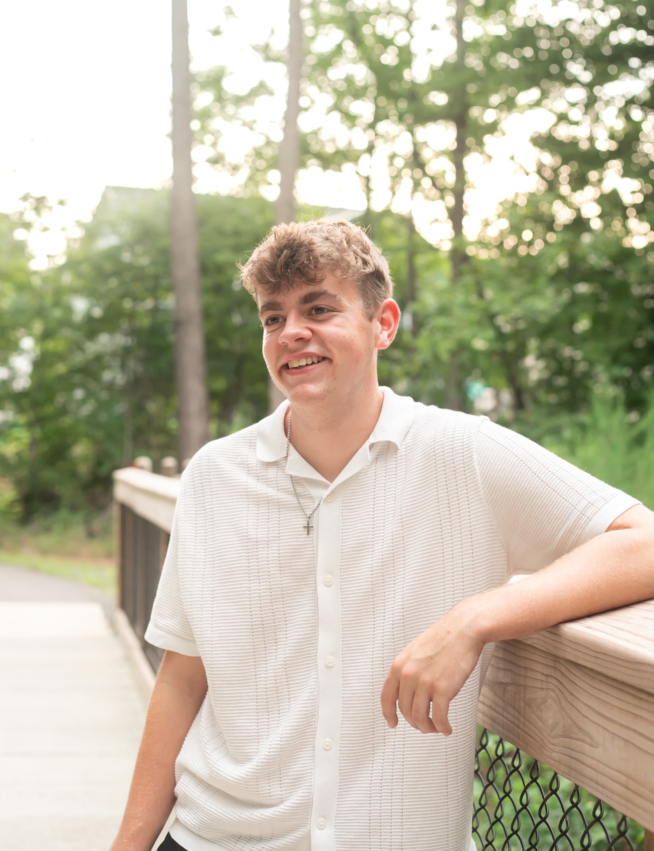 High school senior portrait leaning on a wooden rail in soft evening light